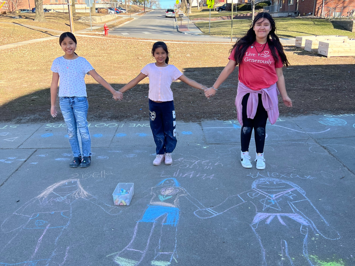 Three girls standing together holding hands by sidewalk chalk drawings.